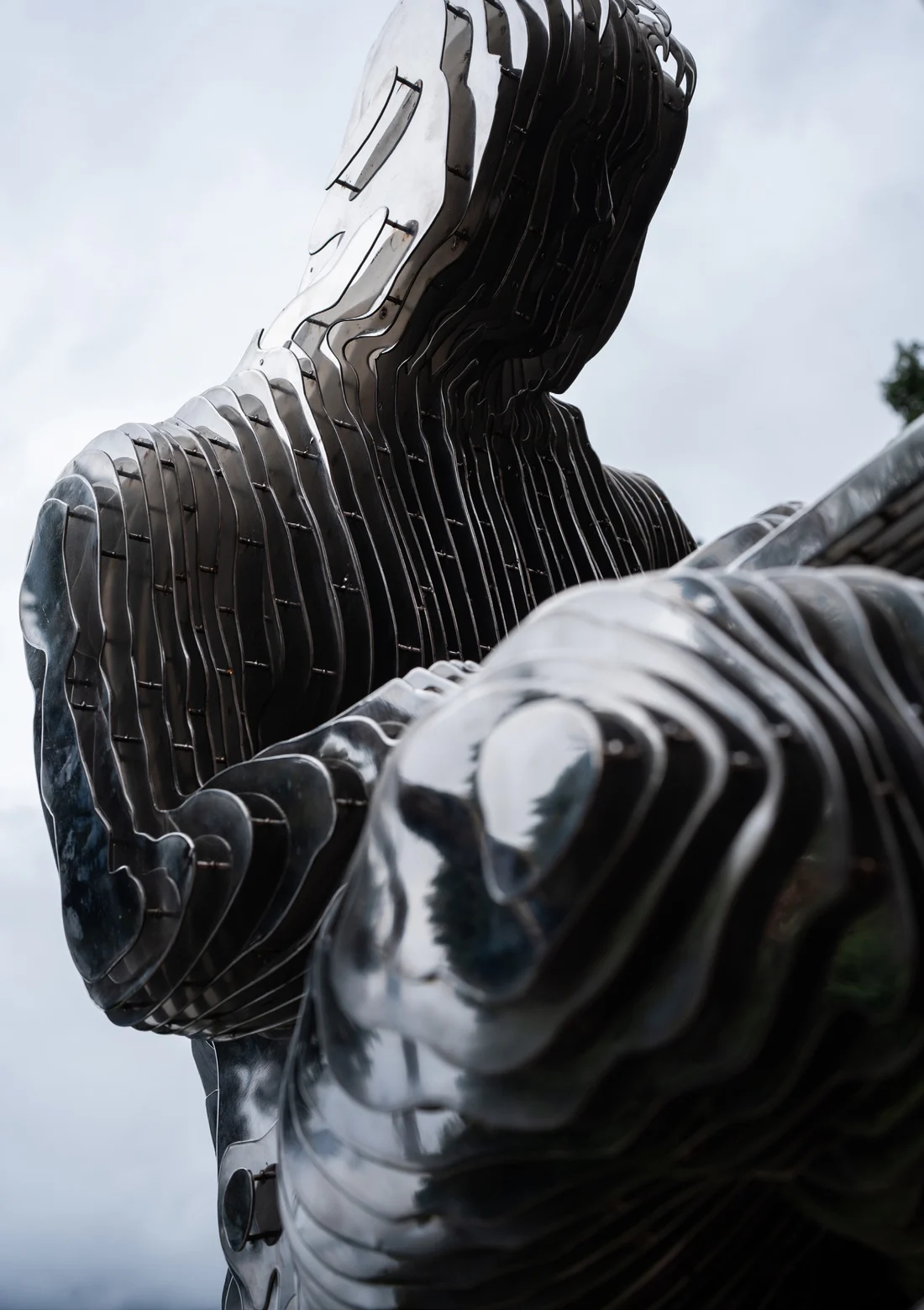 The Satoshi sculpture in Lugano, photographed from below showing its hood, hands and knee.