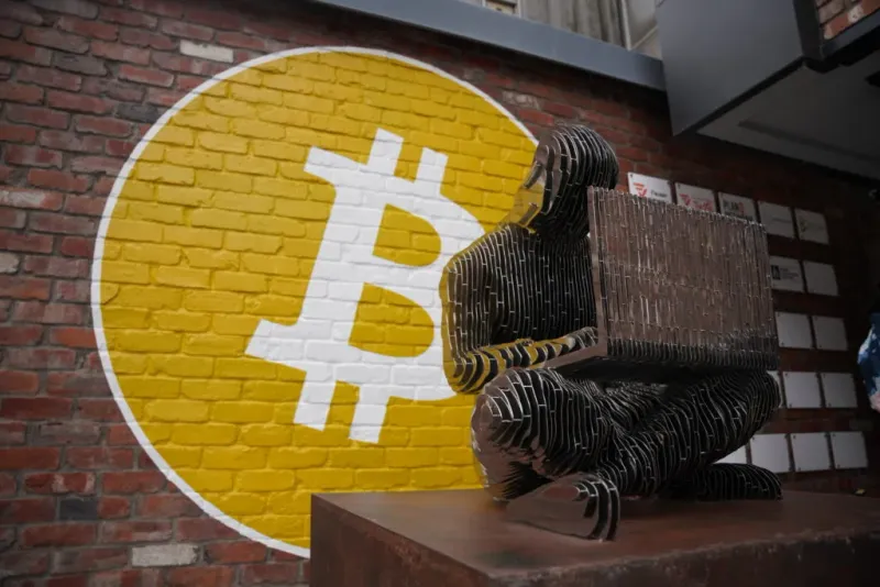 Satoshi sculpture in front of the yellow Bitcoin wall at Tokyo Bitcoin Base.